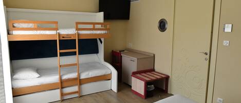 A room with bunk beds, a desk, a television, and a door.