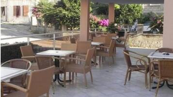 Un patio al aire libre con mesas y sillas, un área de estar cubierta y vistas de los edificios y la vegetación circundante.
