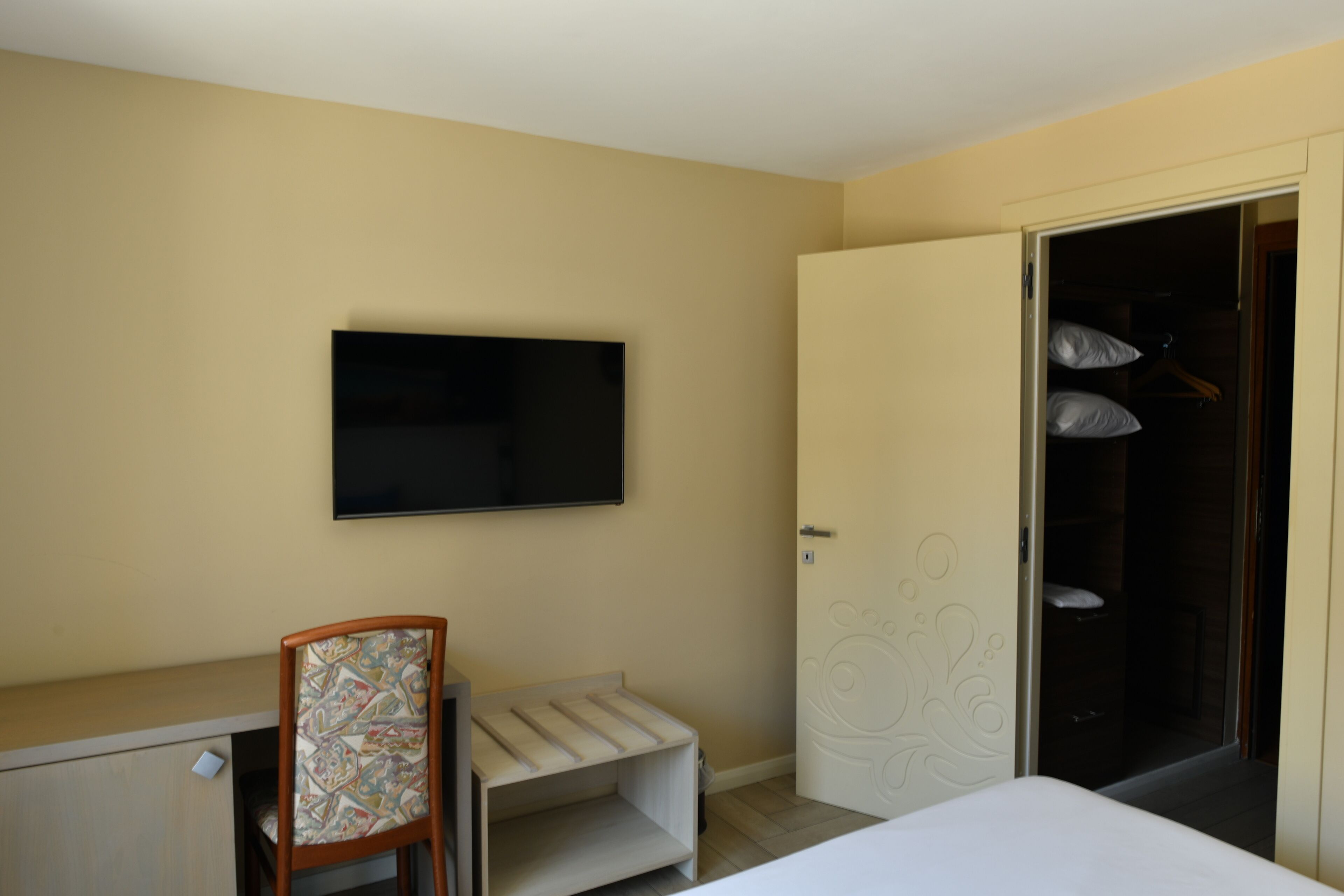 A hotel room with a bed, a desk with a chair, a television, and a wardrobe.