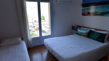 Een slaapkamer met een groot bed, een kleiner bed, een raam met gordijnen en een schilderij aan de muur.
