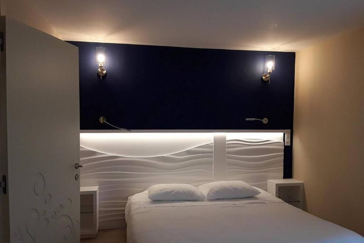 A bedroom with a bed, bedside tables, and wall-mounted lighting.