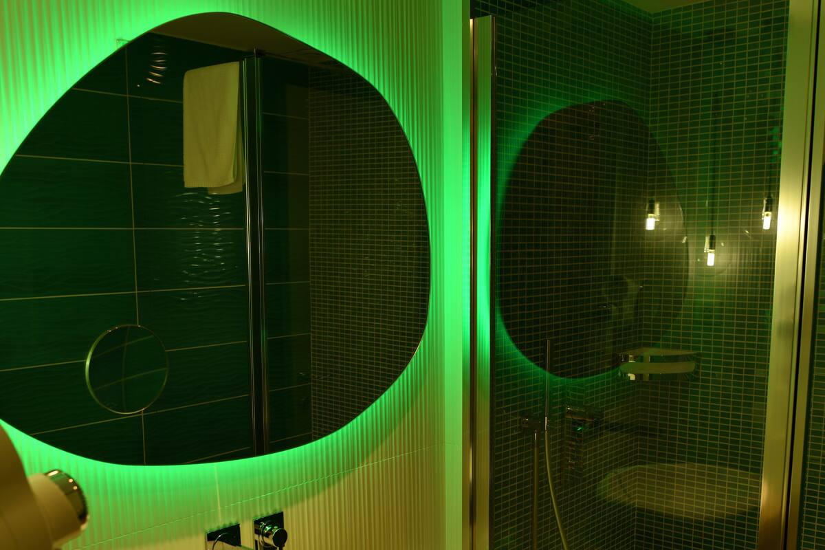 A bathroom with a round mirror, a sink, and a shower area.