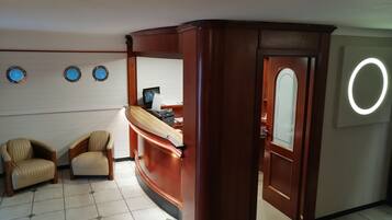 Una zona de recepción con un mostrador de madera curvada, dos sillones color beige y un espejo montado en la pared.