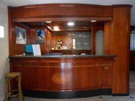 Un mostrador de recepción de madera con una superficie de vidrio, un taburete pequeño y un cartel enmarcado en la pared.