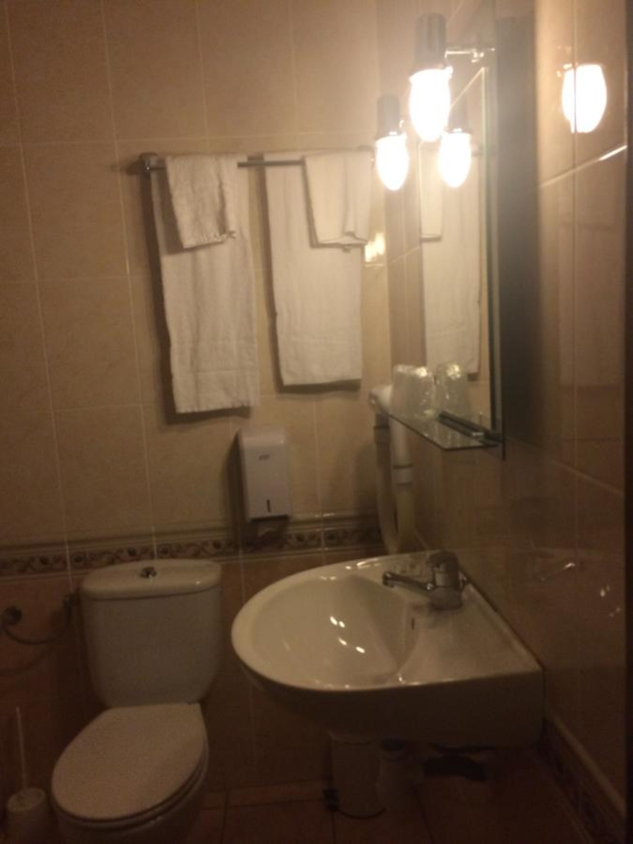 A bathroom with a toilet, sink, and a mirror with lights. There are towels hanging on a rack.