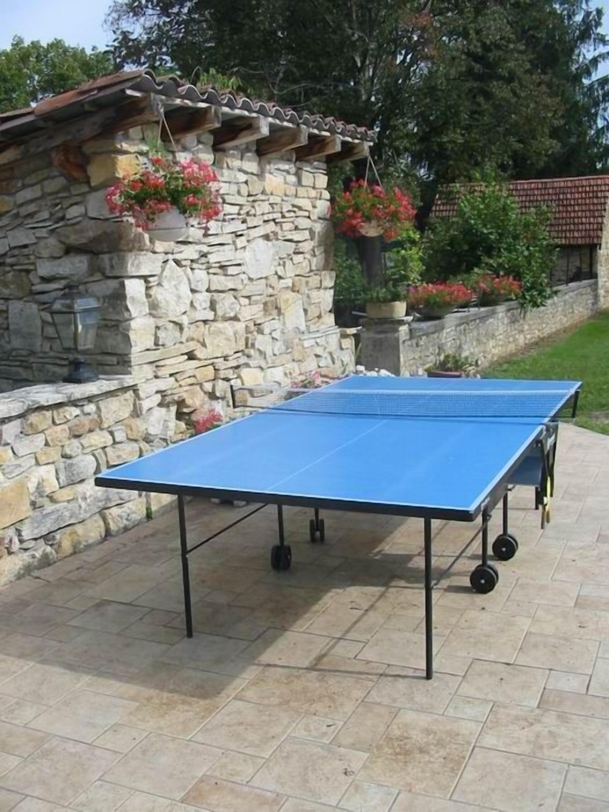 An outdoor ping pong table set up on a patio with stone walls and potted plants.
