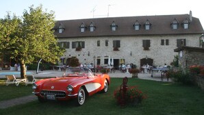 A red convertible car parked in front of a stone building with multiple windows and outdoor seating.