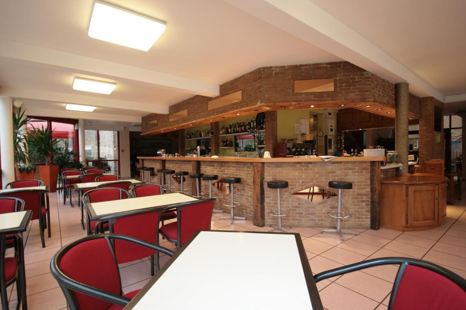 Um restaurante com um balcão de tijolos, cadeiras vermelhas e mesas.