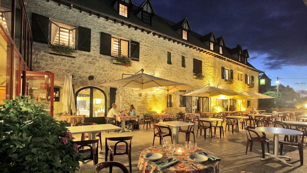 An outdoor dining area with tables and chairs, a stone building with windows, and a night sky.