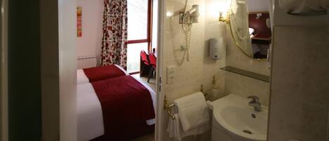 Una habitación de hotel con cama, baño con lavamanos y espejo, y ducha.