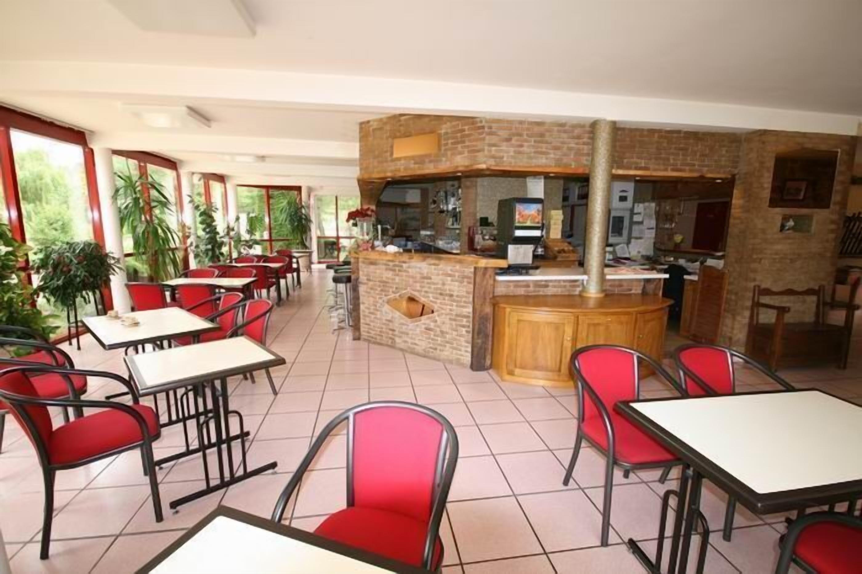A restaurant with red chairs and white tables, a brick counter, and large windows.