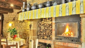 A rustic dining room with a stone fireplace, wooden beams, and a table set for a meal.