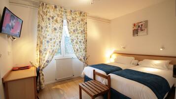 A hotel room with a bed, a desk, a chair, a TV, and a window with floral curtains.