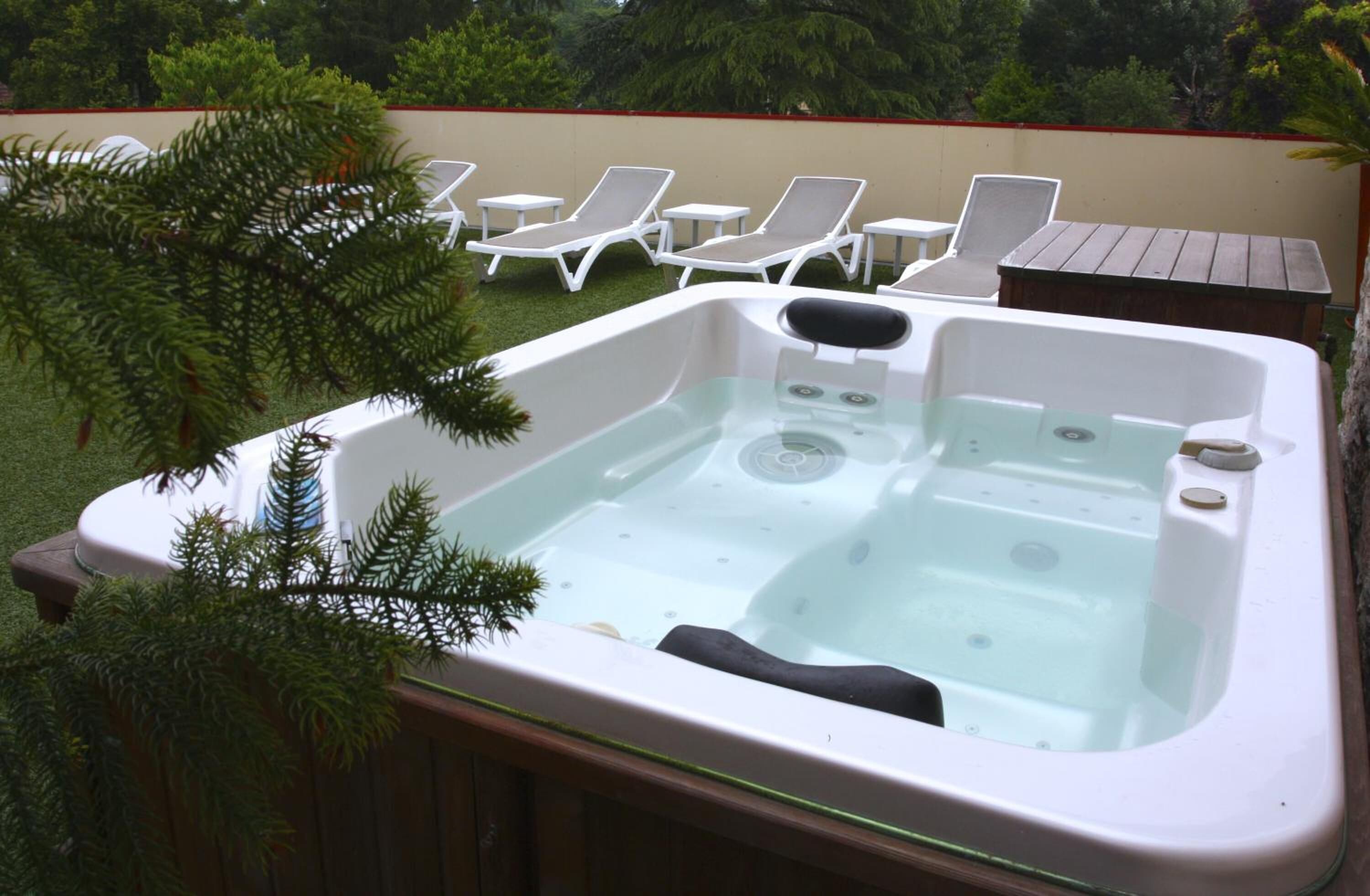 A hot tub with a wooden deck, surrounded by white lounge chairs and a small table.