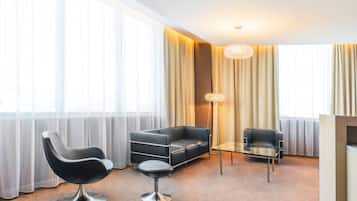 A modern hotel room with a black leather sofa, a black leather chair, a glass coffee table, and a floor lamp.