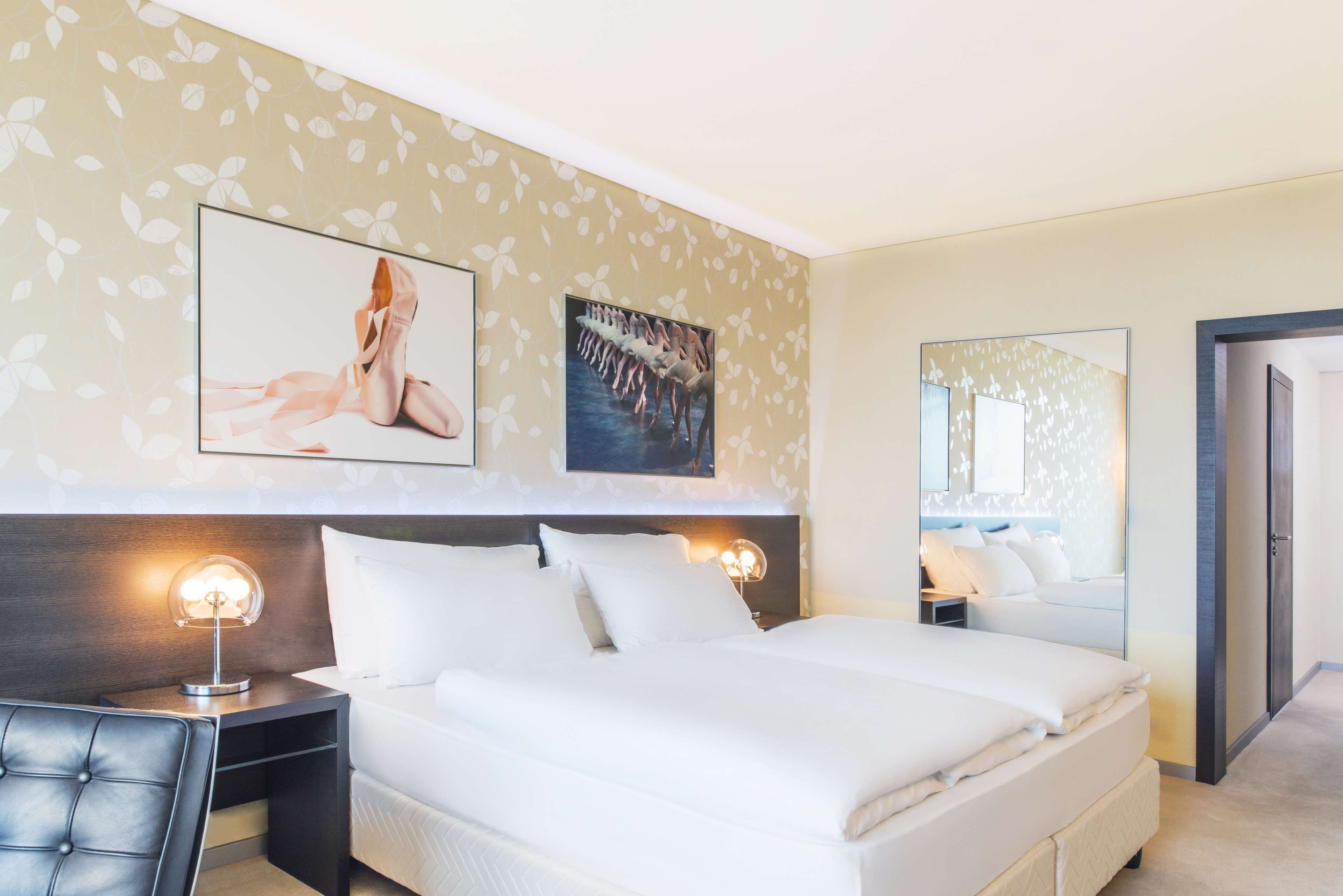 A hotel room with a large bed, two bedside tables with lamps, a chair, and artwork on the walls.