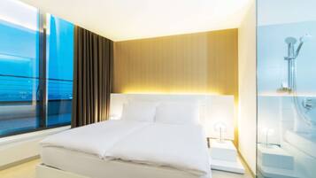 Een moderne hotelkamer met een groot bed, een nachtkastje, een glazen douchecabine en uitzicht op zee door een groot raam.