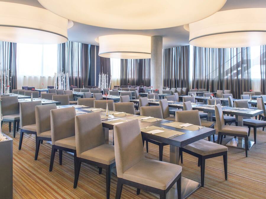Una amplia sala de conferencias con varias mesas y sillas, ventanas grandes con cortinas e iluminación moderna.