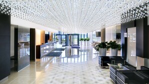 Een moderne lobby met een spiegelende vloer, een receptiebalie en een zithoek met potplanten.