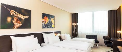 Habitación de hotel con tres camas, un escritorio, una silla y dos lámparas de pared.