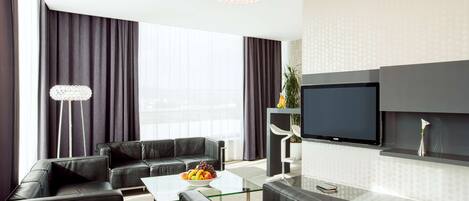 Una sala de estar moderna con un sofá de cuero negro, una mesa de centro de vidrio y un televisor de pantalla plana montado en la pared.