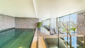 Een binnenzwembad met een glazen barrière, betegelde muren en een loungehoek met ligbedden.