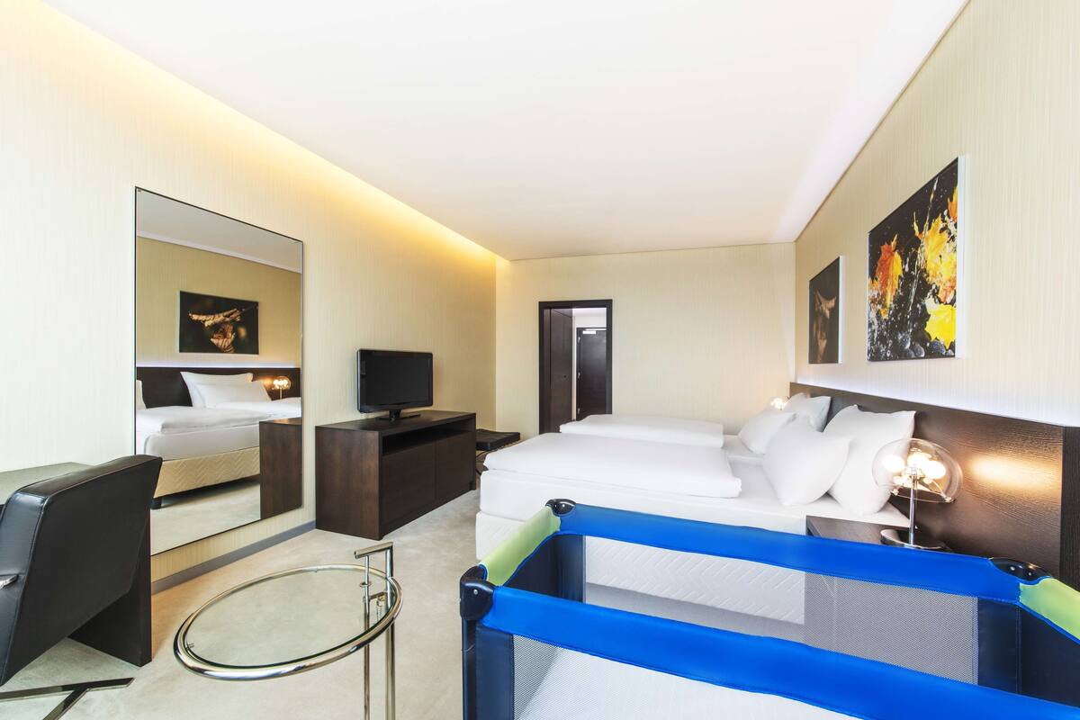 A hotel room with a bed, a desk, a chair, a TV, and artwork on the walls.
