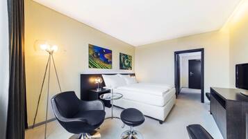Una habitación de hotel con una cama, una silla negra, una mesita, un escritorio y un televisor.