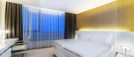 A modern hotel room with a large bed, a desk, and a chair.