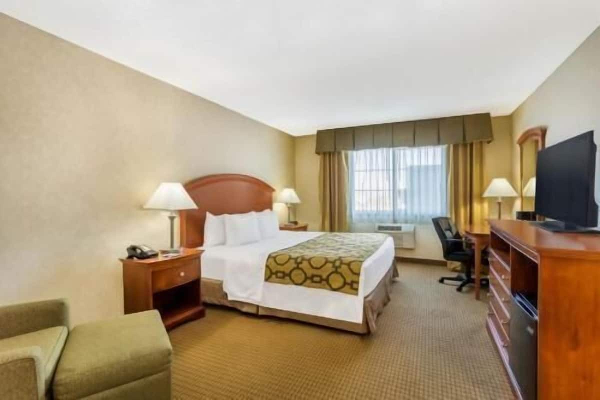 Ein Hotelzimmer mit einem Bett, zwei Nachttischlampen, einem Schreibtisch mit Stuhl, einem Fernseher und einem Sofa.