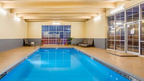 An indoor swimming pool with tiled walls and a tiled floor, two lounge chairs, and a large window with a view. - Baymont by Wyndham Fort Morgan (Fort Morgan)