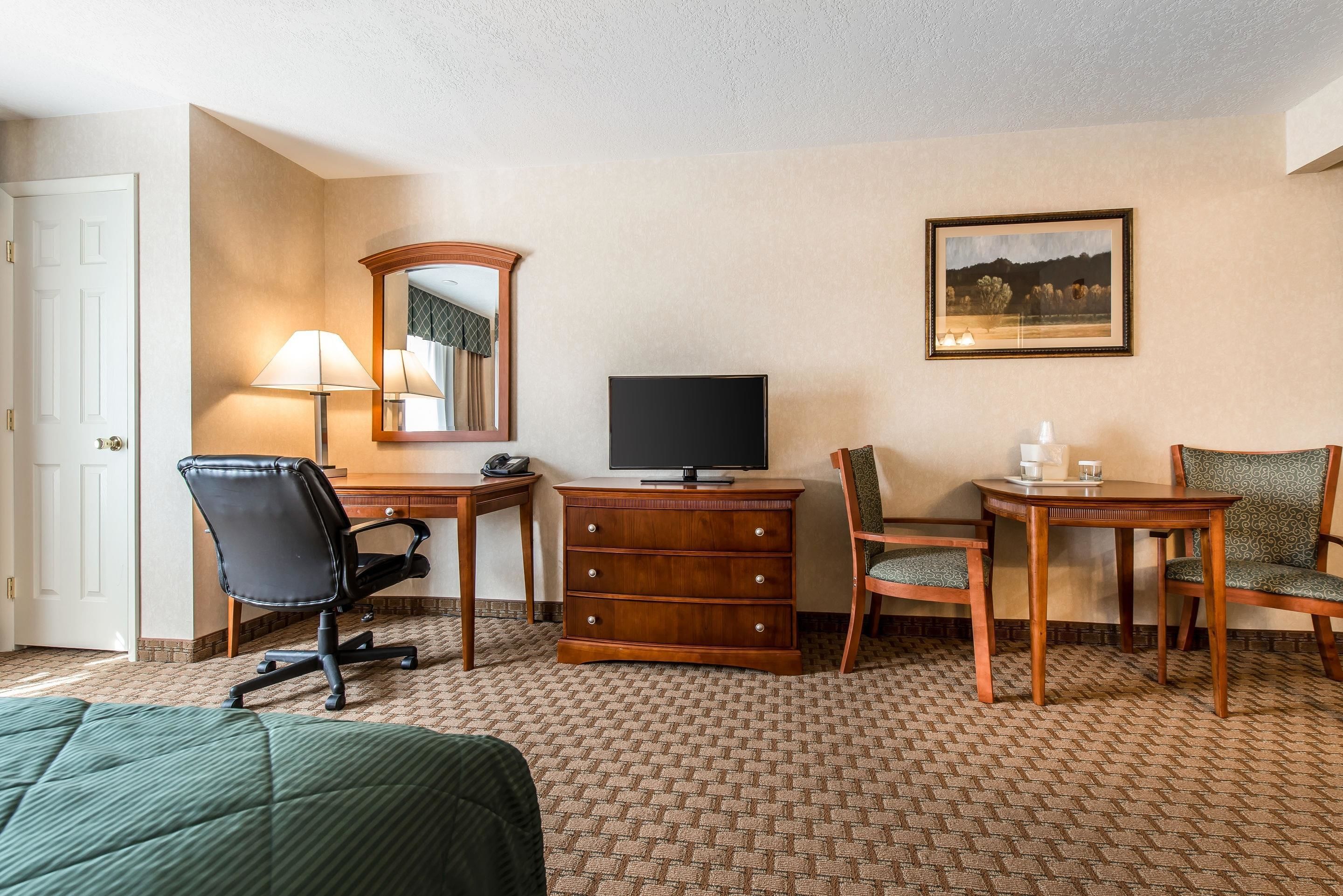 A hotel room with a bed, a desk with a television, a chair, a dresser, and a framed picture on the wall.