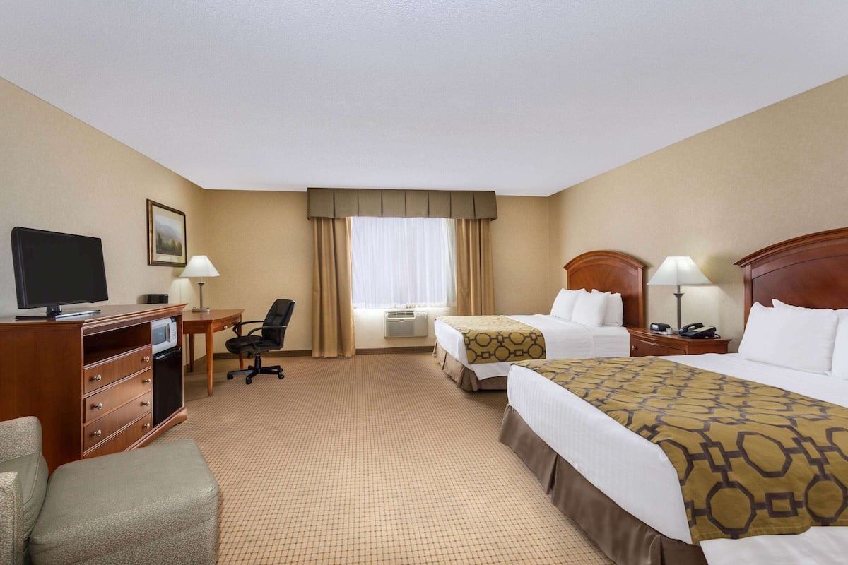 Ein Hotelzimmer mit zwei Betten, einem Schreibtisch mit Computer, einem Fernseher, einem Sessel und einer Lampe.