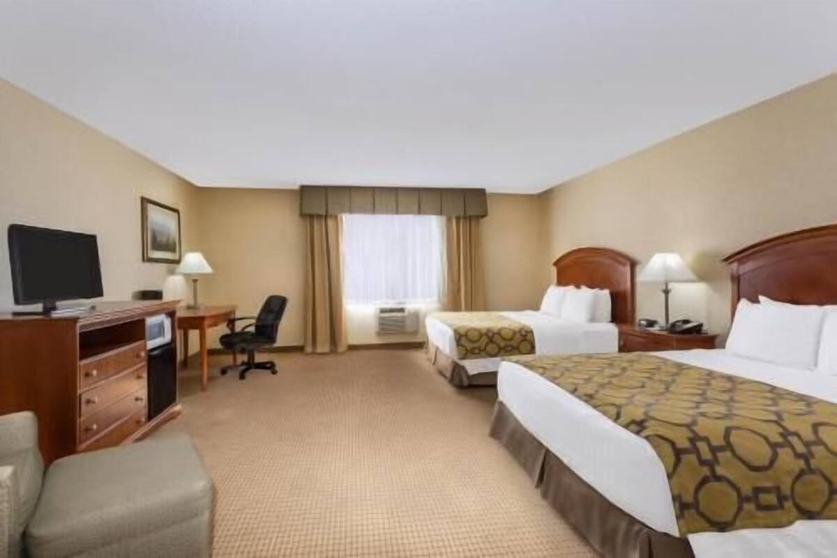 A hotel room with two beds, a desk with a computer, a chair, and a television.