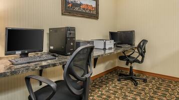 A hotel workspace with two desktop computers, a printer, a keyboard, and two office chairs.