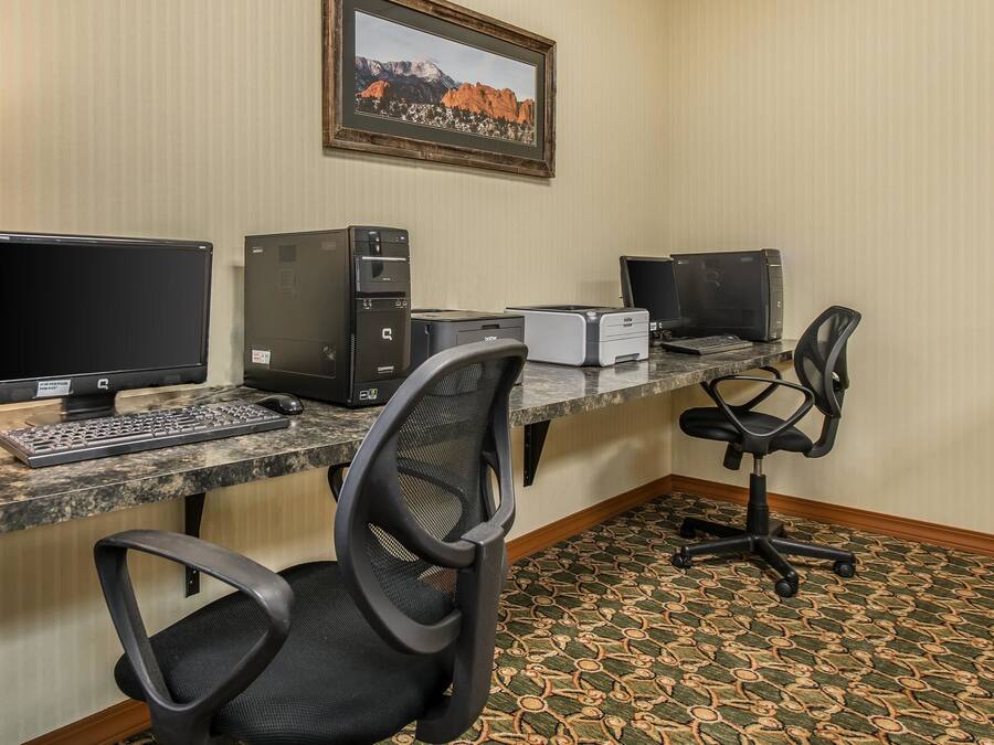 A hotel workspace with two desktop computers, a printer, a keyboard, and two office chairs.