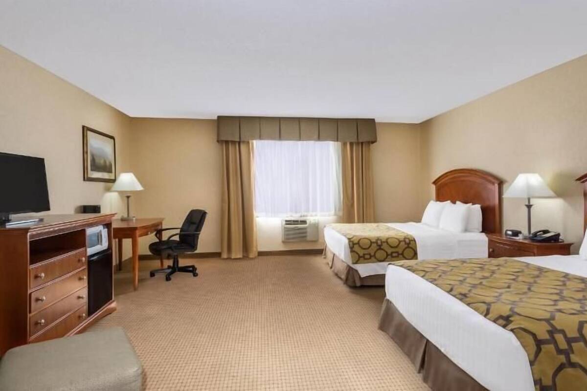 A hotel room with two beds, a desk with a computer, a chair, and a television.