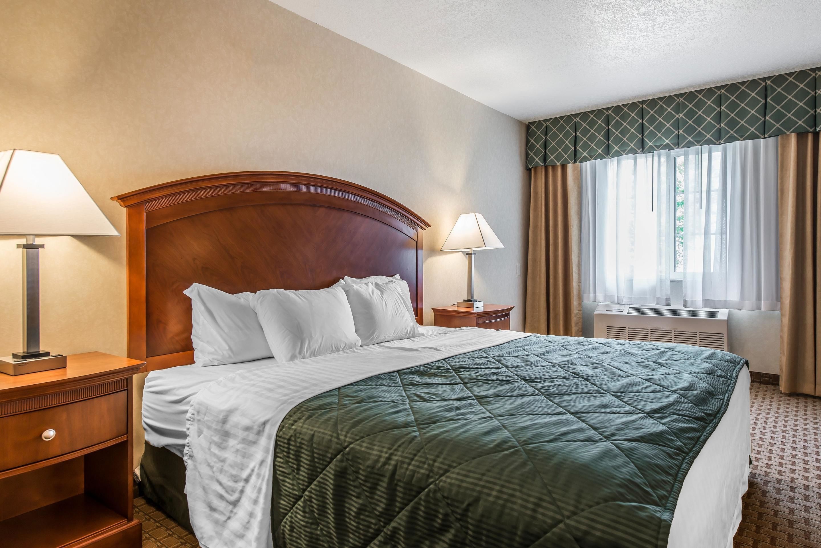 Una habitación de hotel con una cama grande, dos mesitas de noche, una ventana con cortinas y aire acondicionado instalado en la pared.