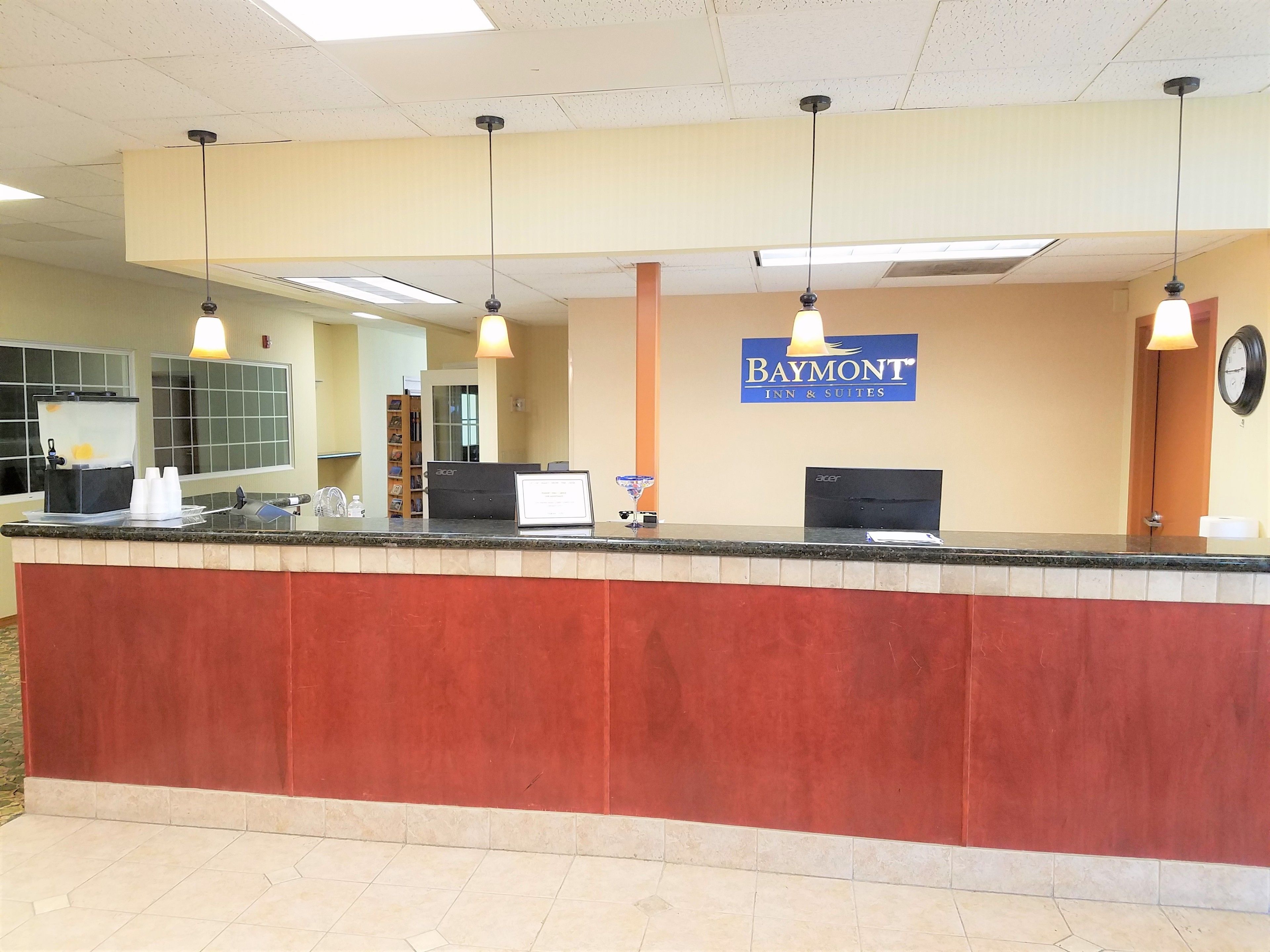 En receptionsdisk med et Baymont Inn & Suites skilt, et ur og en vanddispenser.
