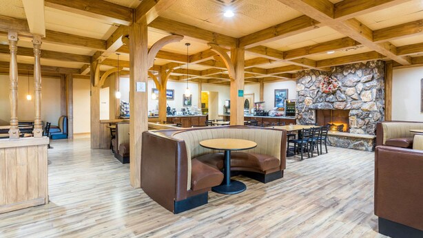 A spacious indoor area with wooden beams and stone walls, featuring seating arrangements and a fireplace. - Baymont by Wyndham Fort Morgan (Fort Morgan)