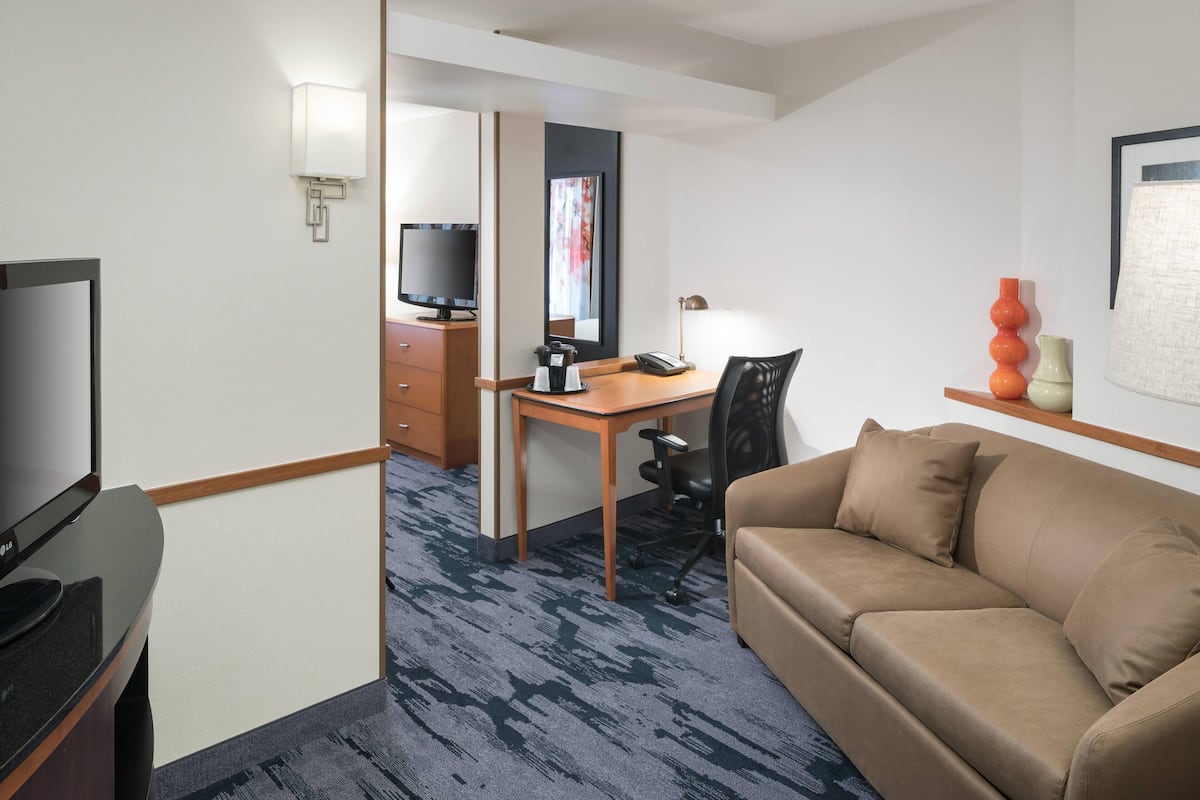 Ein Hotelzimmer mit einer Couch, einem Schreibtisch mit Stuhl, einem Fernseher, einer Kaffeemaschine und einer Lampe.