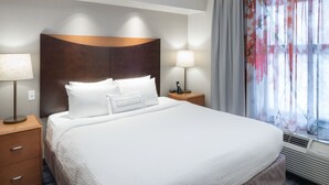 A hotel room with a large bed, two bedside tables, a headboard, and a window with curtains.