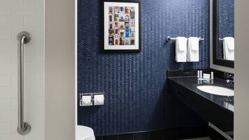 A modern bathroom with a black and white tiled floor, a framed collage of buildings on the wall, a black sink, and a white toilet.