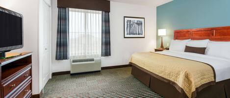 Habitación de hotel con cama, televisor, ventana con cortinas, un cuadro en la pared y piso alfombrado.