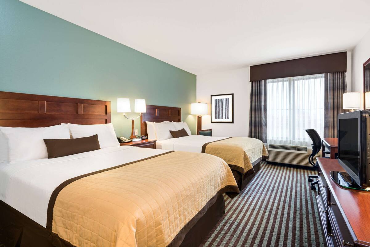 A hotel room with two beds, a desk with a TV, and a large window with curtains.