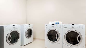Two front-loading washing machines in a laundry room with a plain wall and tiled floor.