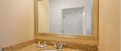 A bathroom with a granite countertop sink, a mirror, and a shower visible in the reflection.
