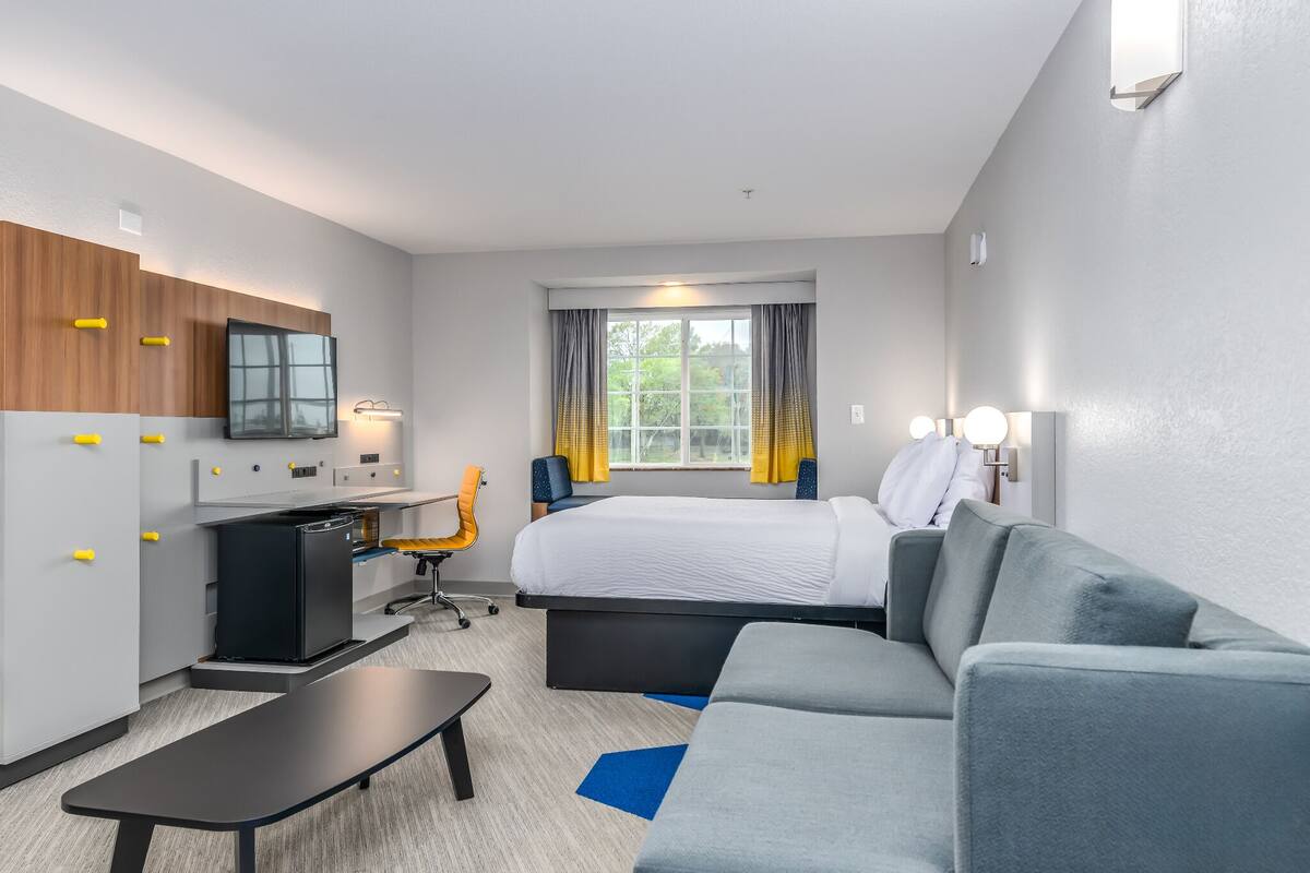 A hotel room with a bed, a desk, a chair, a sofa, and a small table.