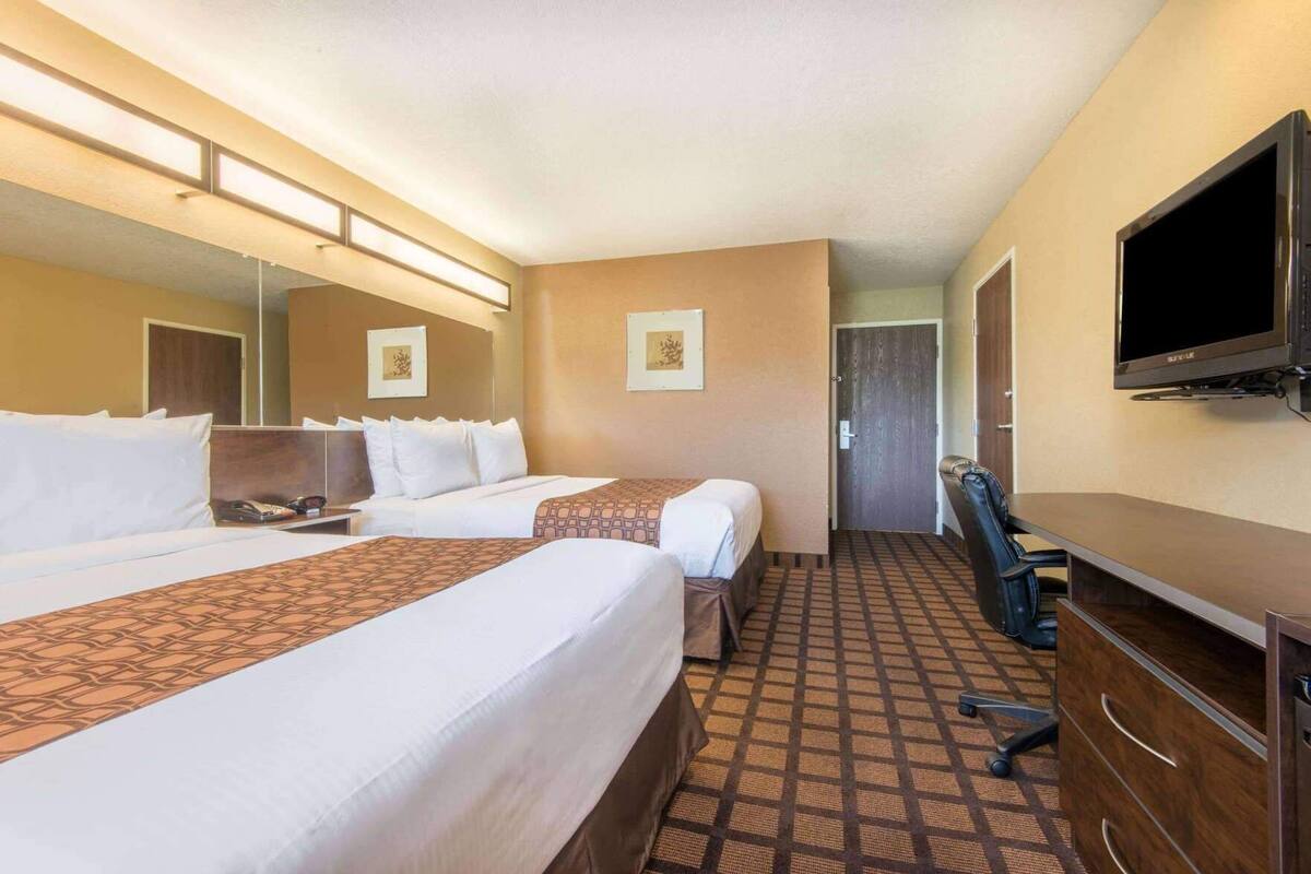 A hotel room with two beds, a desk, a chair, a television, and a door leading to another room.