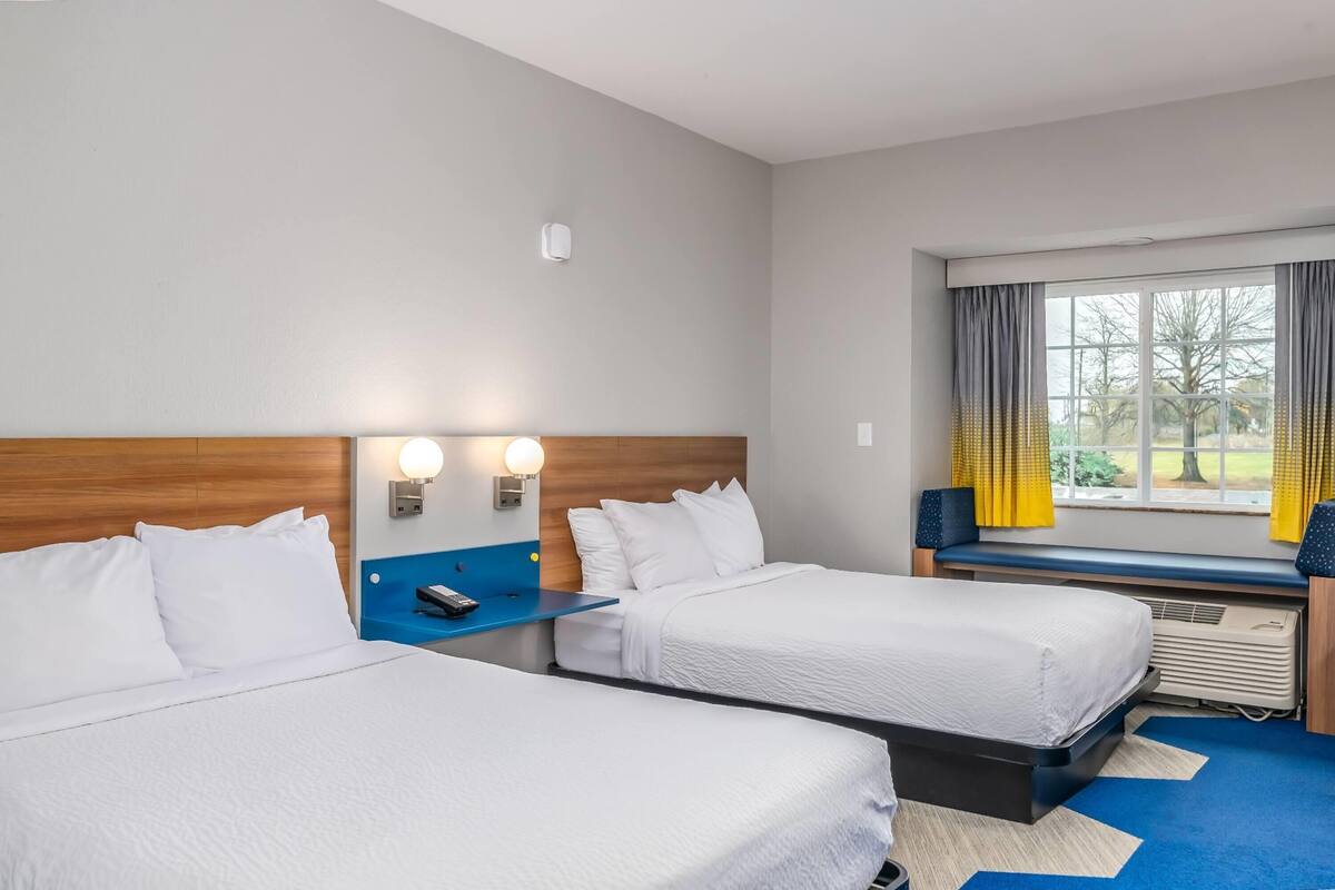 A hotel room with two beds, a wooden headboard, a window with curtains, and a blue carpet.
